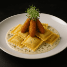 Assiette de ravioli dans une sauce charcutière crémeuse, garnis de trois cornichons frits croustillants et de pousses de luzerne