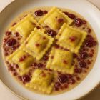 Plat de ravioli au canard confit servi avec une sauce au poivre et canneberges, présentation style restaurant étoilé.