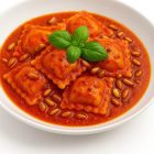 Plat de ravioli portugais nappés d’une sauce piri-piri légère avec pignons de pin grillés, présentation gourmet.