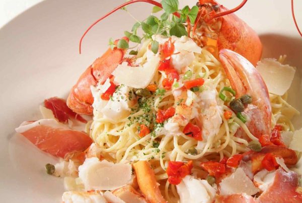 Plat de spaghetti au homard garni de chair de homard, copeaux de parmesan et herbes fraîches, présentation gastronomique.