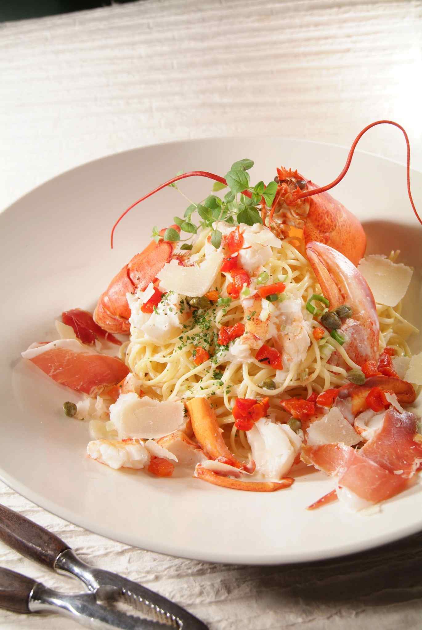 Plat de spaghetti au homard garni de chair de homard, copeaux de parmesan et herbes fraîches, présentation gastronomique.